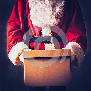 Santa Claus as a delivery man holds a parcel, a cardboard gift box with space for text