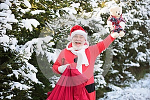 Santa Claus with a bag of Christmas gifts comes in the snow forest.