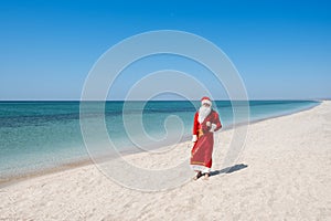 Santa Claus with a bag of gifts walking on the sandy beach