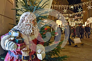 Santa Claus and beautiful Christmas decorations at night in the city center. Shopping rush during holidays concept, long exposure