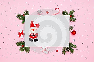 Santa Claus on blank white paper in frame of natural fir tree branches, gifts and decorations on pastel pink flat lay