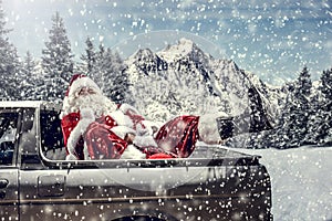 Santa Claus in a car driving to deliver some christmas presents on a sunny winter day. Blurred mountain forest background.