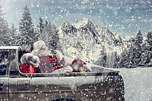 Santa Claus in a car driving to deliver some christmas presents on a sunny winter day. Blurred mountain forest background.