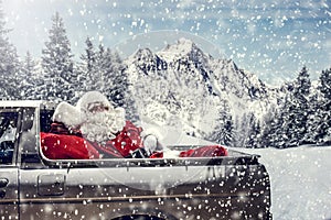 Santa Claus in a car driving to deliver some christmas presents on a sunny winter day. Blurred mountain forest background.