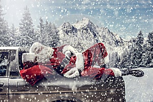 Santa Claus in a car driving to deliver some christmas presents on a sunny winter day. Blurred mountain forest background.