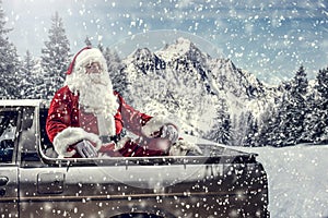 Santa Claus in a car driving to deliver some christmas presents on a sunny winter day. Blurred mountain forest background.