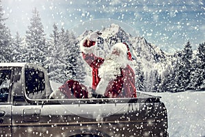 Santa Claus in a car driving to deliver some christmas presents on a sunny winter day. Blurred mountain forest background.