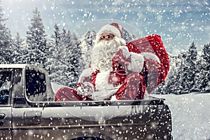 Santa Claus in a car driving to deliver some christmas presents on a sunny winter day. Blurred mountain forest background.