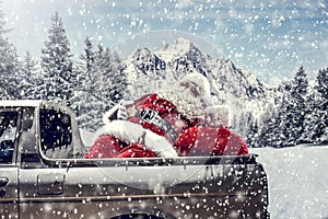 Santa Claus in a car driving to deliver some christmas presents on a sunny winter day. Blurred mountain forest background.