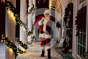 Santa Claus carrying a big sack of gifts outdoors, near house.