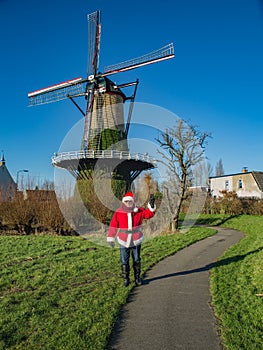 Santa Claus celebrate Christmas, hand of two fingers up. Beautiful view of picturesque village with mill in sunny winter day.