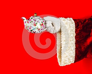 Santa Claus in celebration. Festive tea. The hand of Santa Claus holds a porcelain teapot with a floral pattern on a red