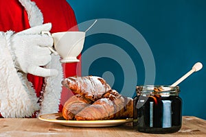 Santa Claus in celebration. Tea or coffee drinking with croissants and honey. Happy and delicious Christmas holiday