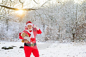 Santa Claus on Christmas Eve is carrying presents to children in a bag on snow landscape.