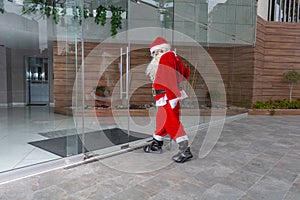 Santa Claus at Christmas opens a glass door of a modern building to enter