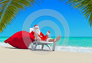 Santa Claus with Christmas sack on deckchair at palm beach