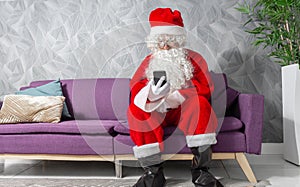 Santa Claus at Christmas sitting on a couch checking his cell phone