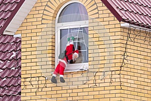 Santa Claus climbing up a wall into a window. Traditional Christmas decoration