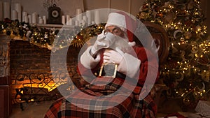 Santa Claus covered with a plaid blanket rests in hut with a hot tea with lemon. Relaxing Santa Claus in sofa chair near