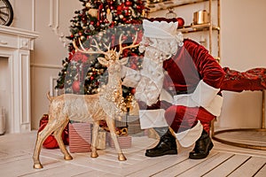 Santa Claus and deer near the fireplace and christmas tree with gifts. New year and Merry Christmas , happy holidays concept