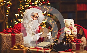 Santa Claus at desk with letters, gifts near Christmas tree