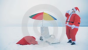Santa Claus is drinking and dancing near a deck-chair and an umbrella