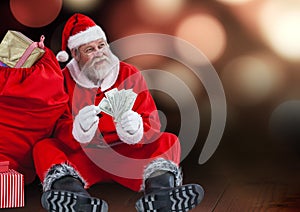 Santa claus with gift sack holding dollars while sitting on wooden plank