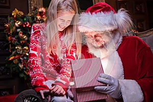 Santa Claus and girl opening Christmas gift near Christmas tree. Magic fulfillment of desires wishes