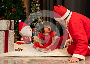 Santa Claus with girl toddler sitting together on floor at home. Christmas celebration concept
