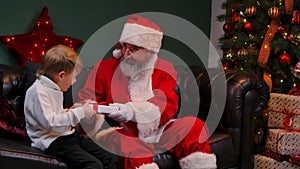Santa Claus gives a cherished gift to a little boy, the child rejoices and hugs the magic grandfather. Holidays and