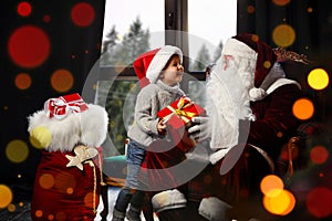 Santa Claus giving Christmas gift to little boy near window