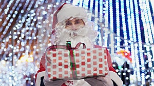 Santa Claus giving a gift box on the background of bright Christmas garlands