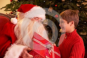 Santa Claus Giving Gift To Boy In Front Of Christm