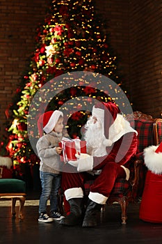 Santa Claus giving present to little boy near Christmas tree