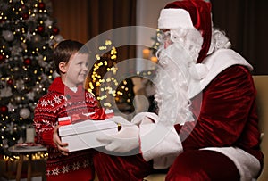 Santa Claus giving present to little boy in room decorated for Christmas