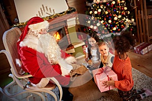 Santa Claus giving a present to a little cute girl in front of h