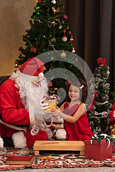 Santa Claus giving present to little cute girl near Christmar tree. Cozy warm winter evening at home. Celebrate holiday Christmas