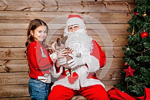 Santa Claus giving a present to a little cute girl near Christmas tree at home