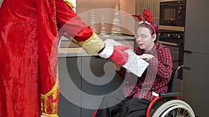 Santa Claus is giving presents to Girl with Cerebral Palsy in a Wheelchair at home. Merry Christmas and Happy New Year