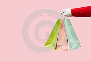 Santa Claus hand holding colorful shopping bags on pink isolated background