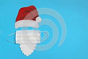 Santa Claus hat and beard with medical mask on light blue background. Christmas and New Year concept