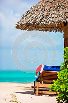 Santa Claus Hat on chair near tropical beach with turquoise sea water and white sand. Christmas vacation concept