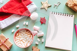 Santa claus hat, christmas decorations, coffee with marshmallows, gifts and notepad with place for text