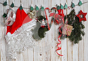 Santa Claus hat and Christmas tree decorations hang on clothespins on a rope against a wooden background with fir branches and