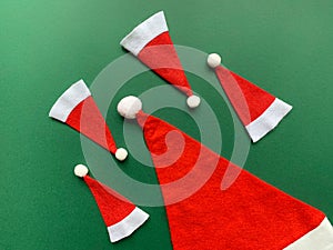 Santa Claus hat and few small Christmas hats on green background. Flat lay Christmas background