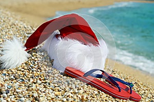 Santa Claus hat and flip flops Ð¾n sand.