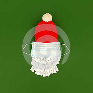 Santa Claus hat and paper beard with medical  face mask on classic green background, creative minimal concept of Christmas and New