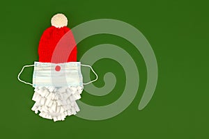 Santa Claus hat and paper beard with medical  face mask on classic green background, creative minimal concept of Christmas and New