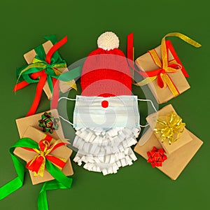 Santa Claus hat and paper beard with medical face mask and gift boxes on classic green background, creative minimal concept of