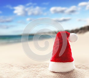 Santa Claus hat on white sand of tropical beach. Christmas or New Year`s vacation concept.